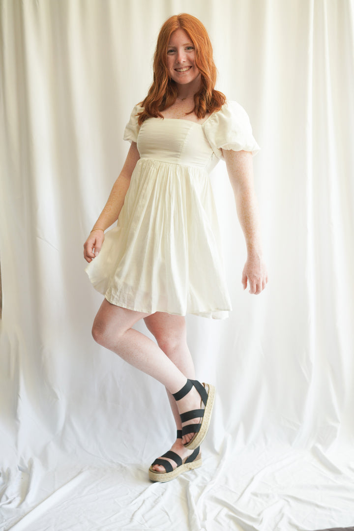 Women wearing white linen babydoll dress. puff sleeves, linen fabric, and smocked back detailing