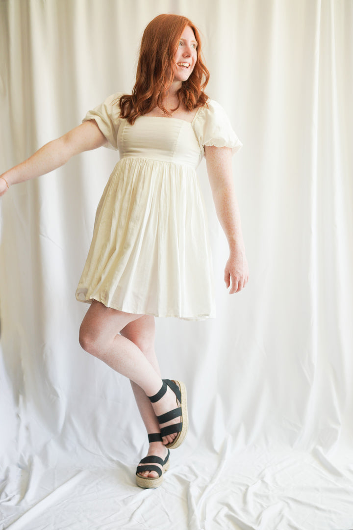 Women wearing white linen babydoll dress. puff sleeves, linen fabric, and smocked back detailing