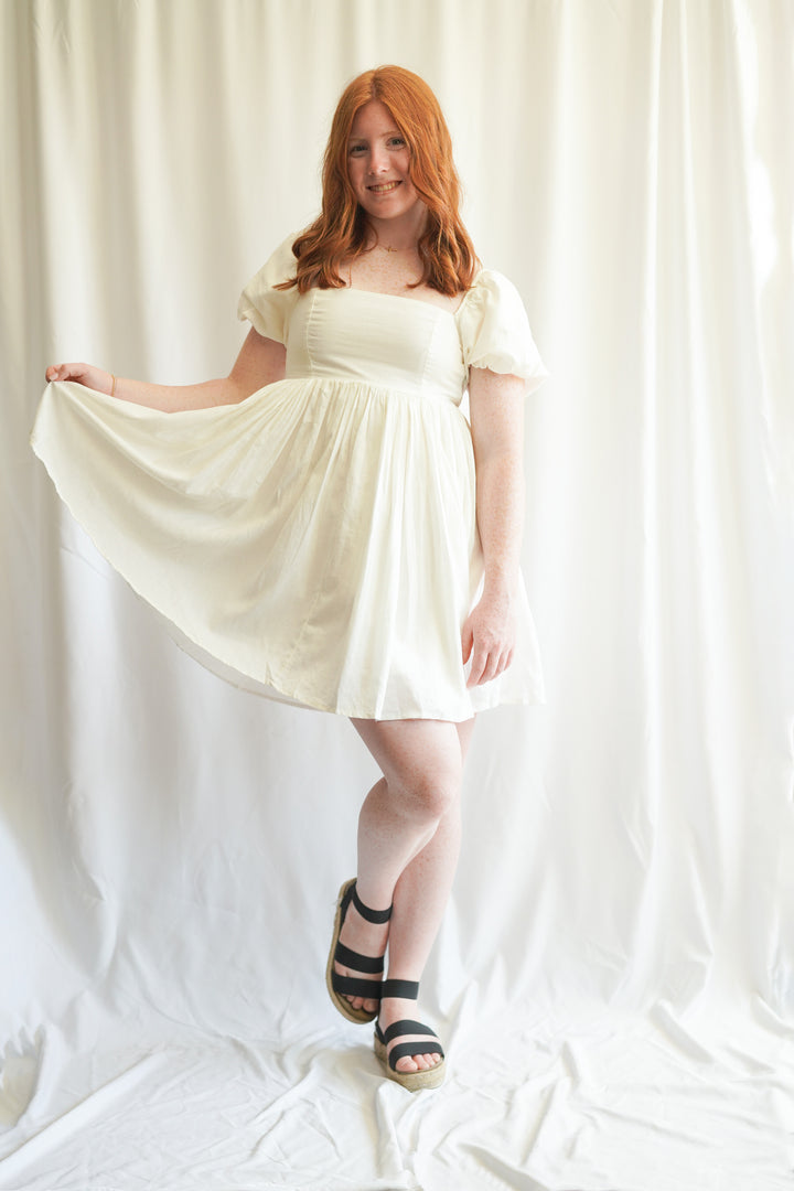 Women wearing white linen babydoll dress. puff sleeves, linen fabric, and smocked back detailing