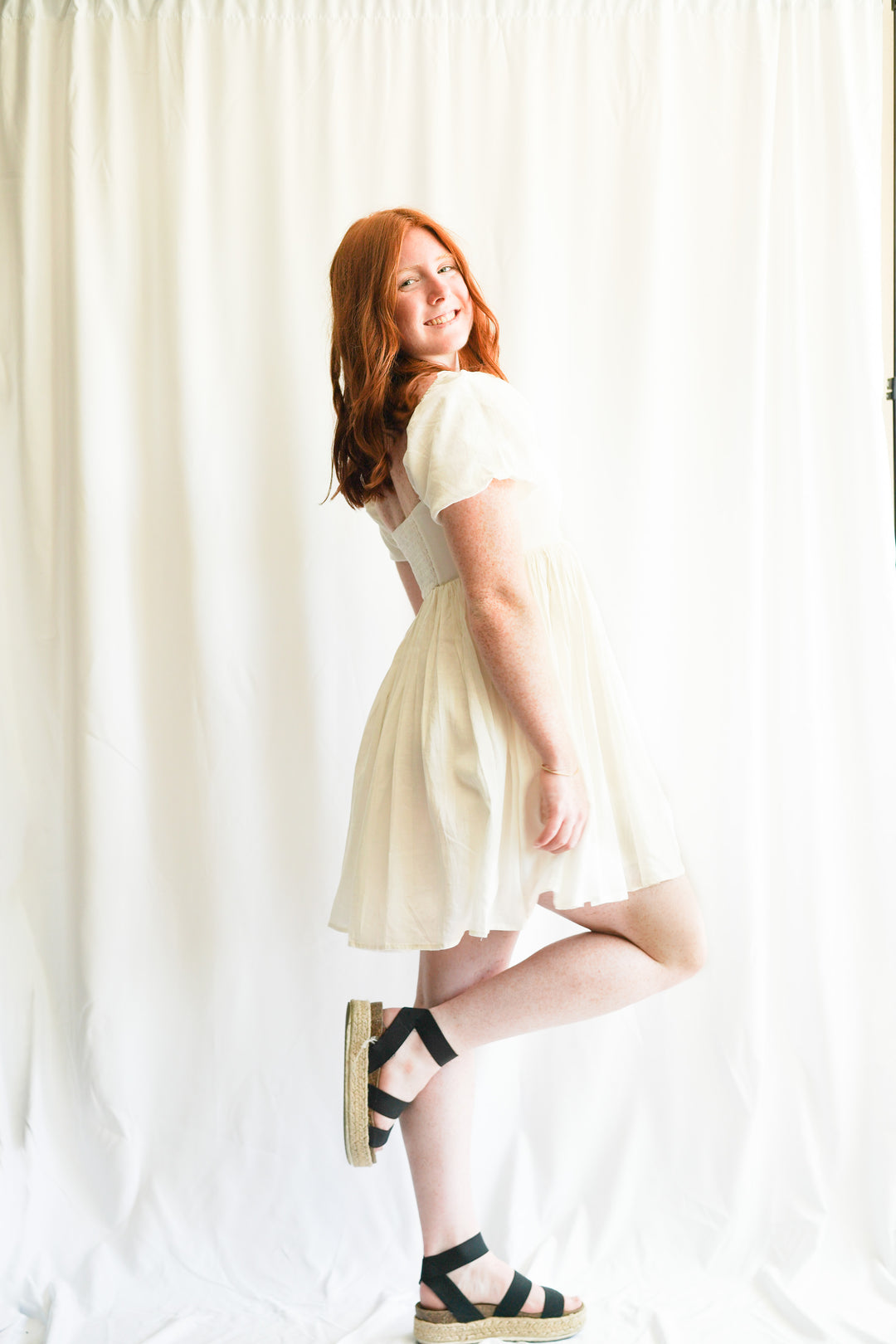 Women wearing white linen babydoll dress. puff sleeves, linen fabric, and smocked back detailing