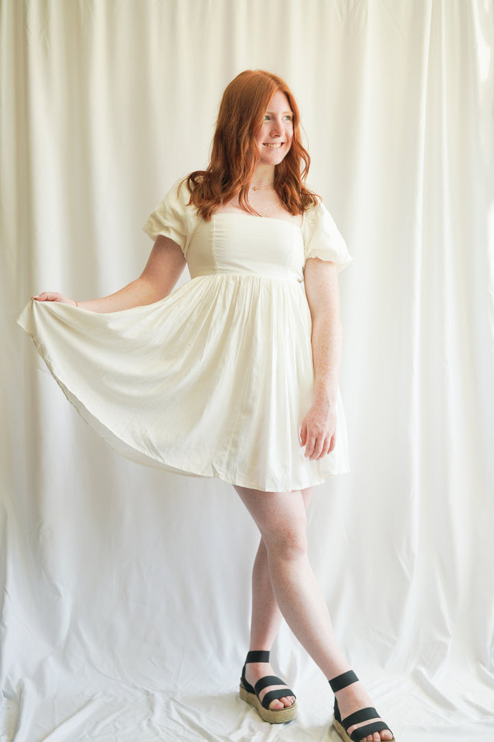 Women wearing white linen babydoll dress. puff sleeves, linen fabric, and smocked back detailing